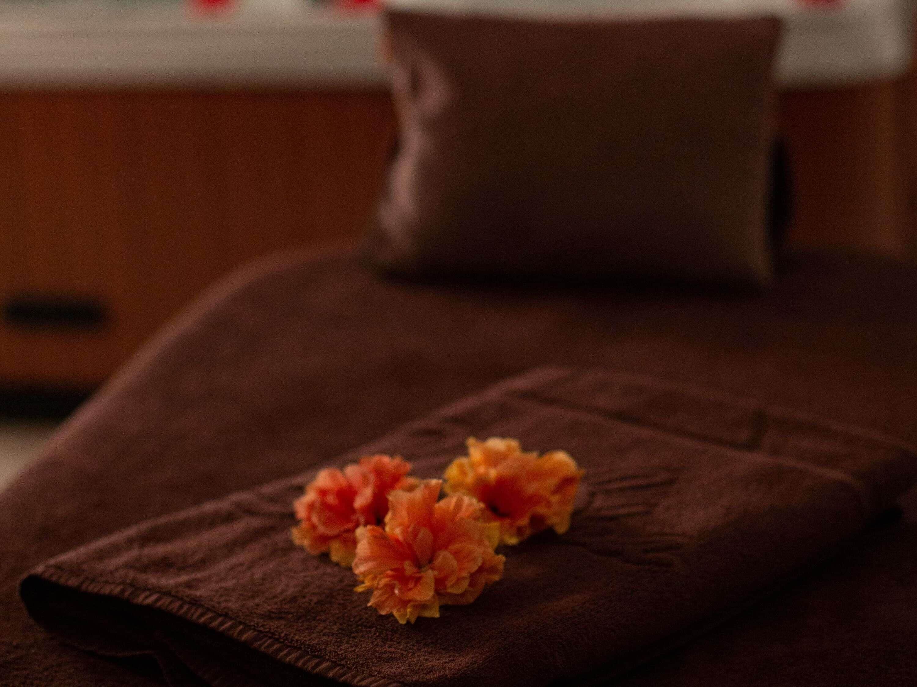 Un lettino da massaggio con un asciugamano marrone e fiori arancioni.
