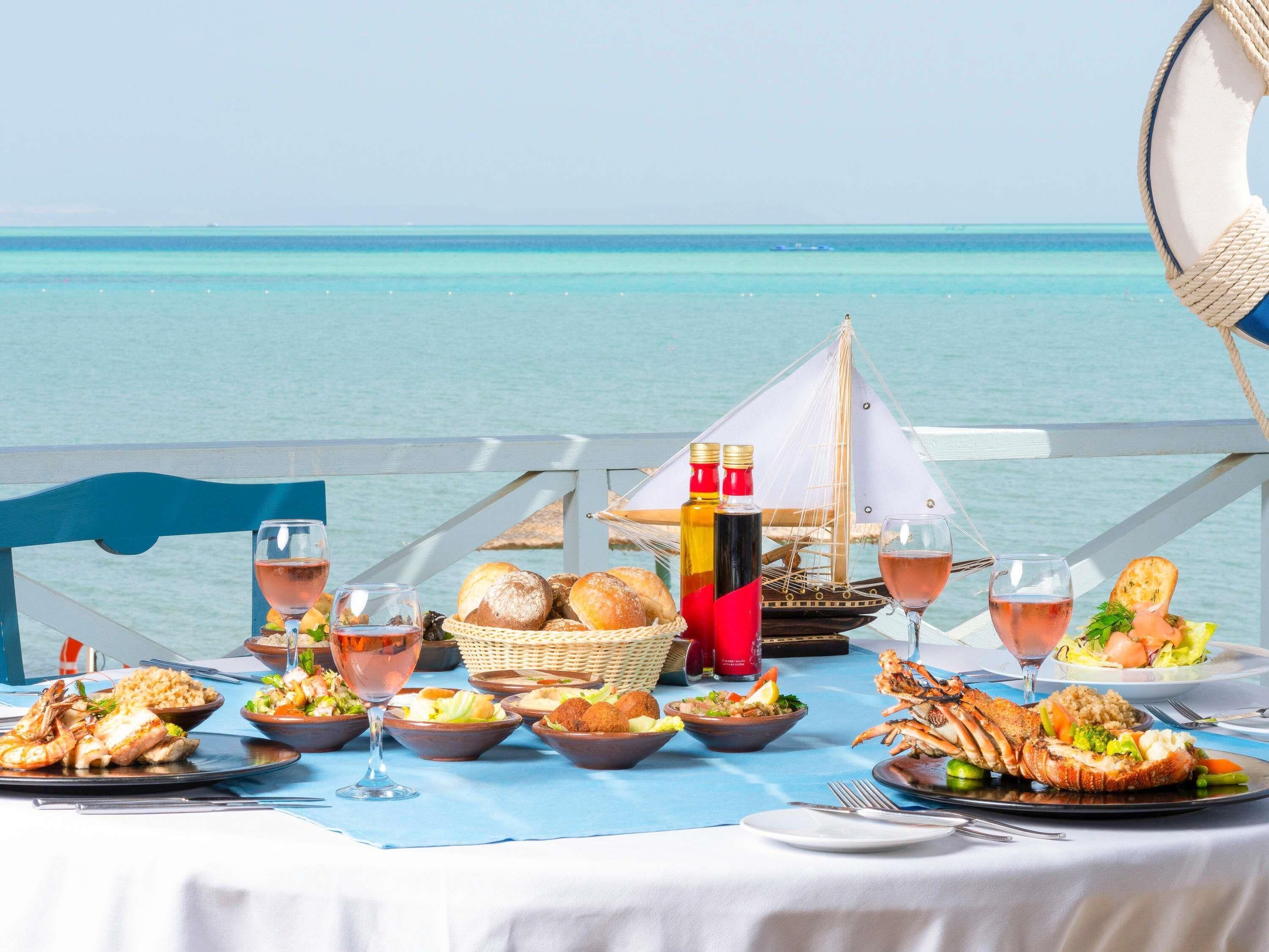 A table set with seafood dishes, glasses of wine, and a view of the ocean.