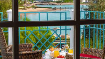 Un balcone con sedie in vimini, un tavolo imbandito con prodotti per la colazione e vista sulla spiaggia e sulla piscina.