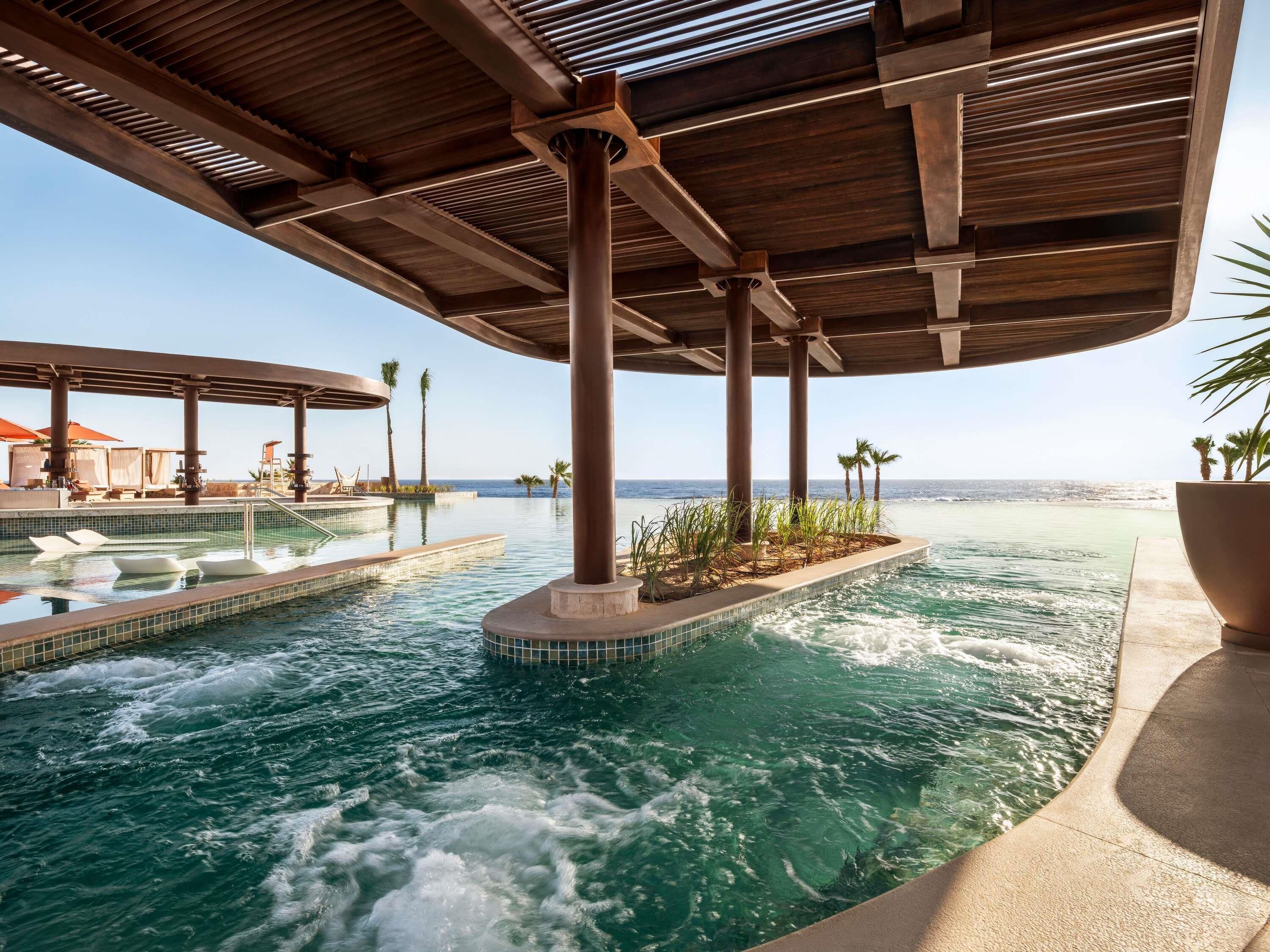 Un área de piscina con un toldo de madera, un jacuzzi y vista al océano.
