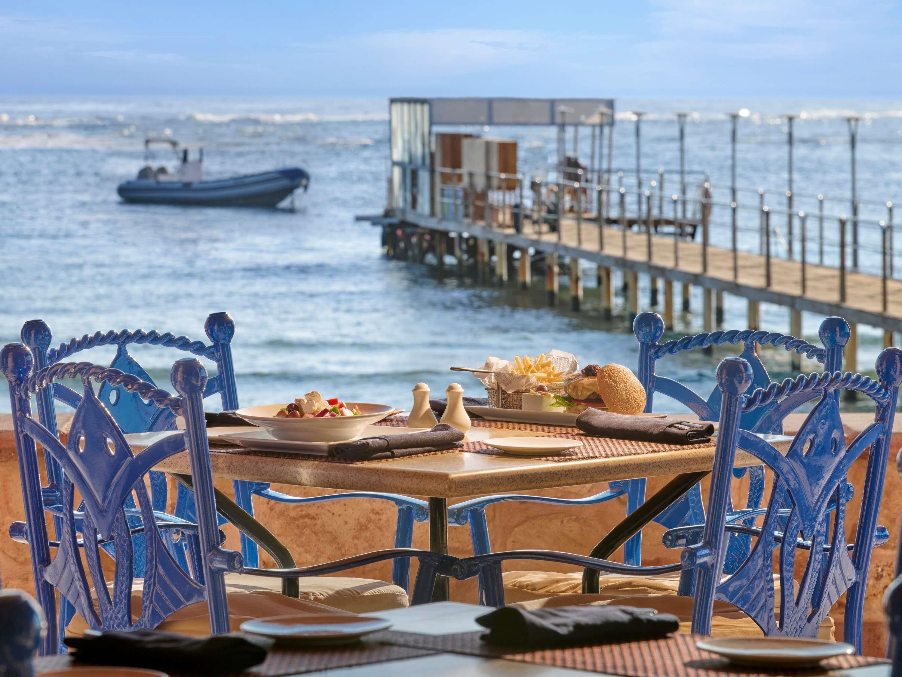 A dining table with chairs and a view of the sea and a pier.