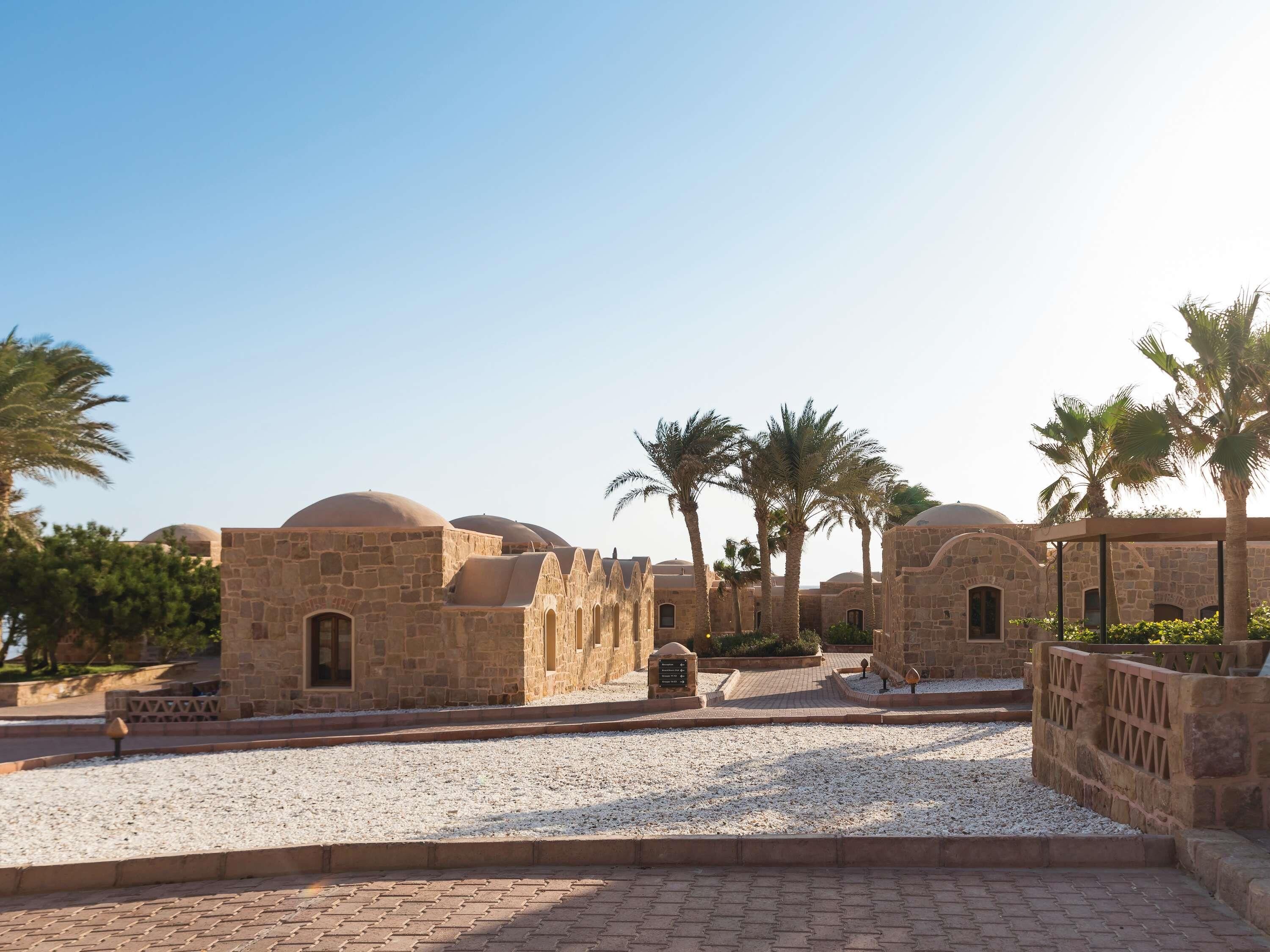 A courtyard with stone buildings, palm trees, and a gravel path.