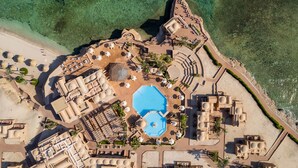 Vue aérienne d’un complexe hôtelier doté d’une piscine centrale, de plusieurs espaces de détente et d’une plage.