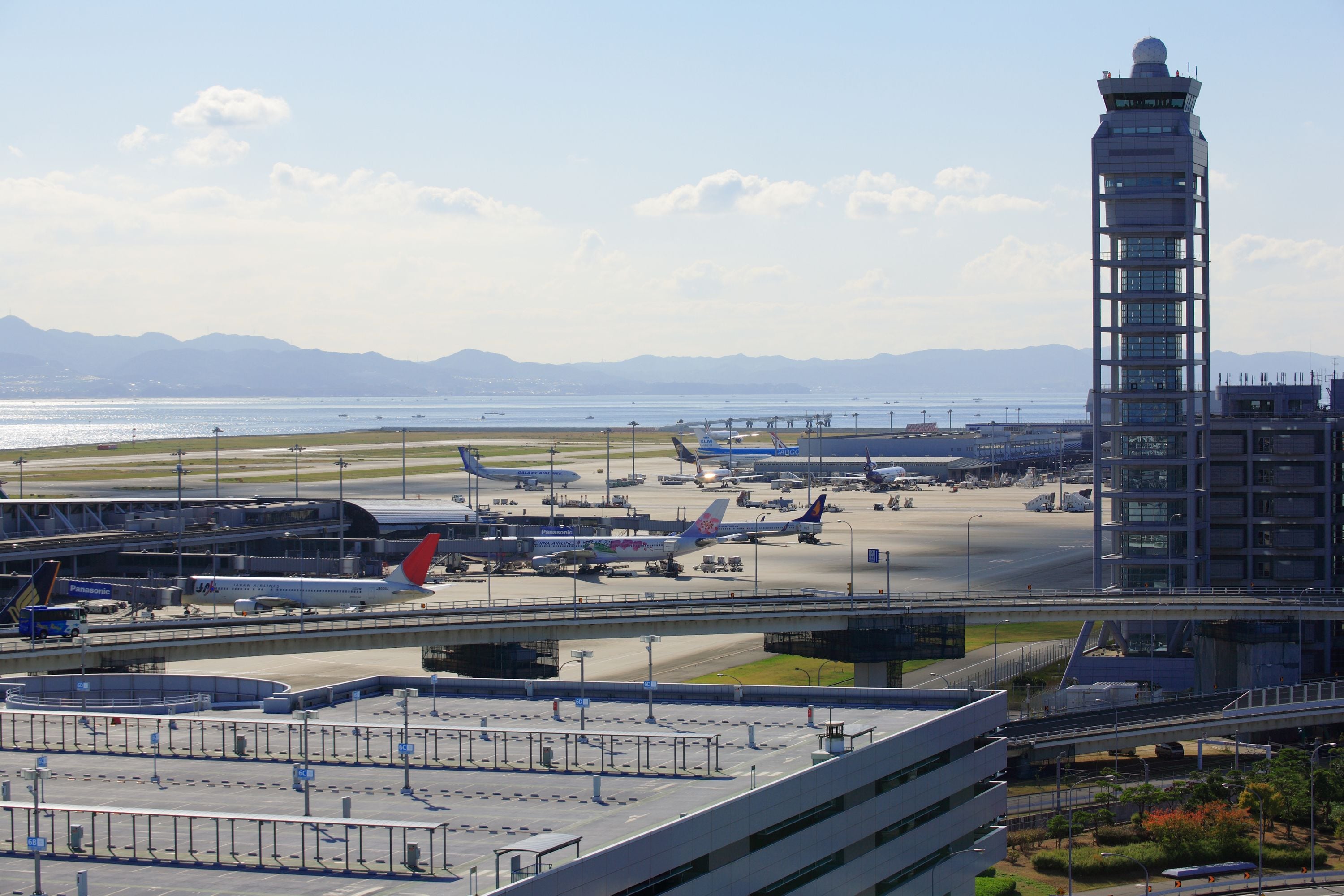 An airport with multiple airplanes parked, a control tower, and a modern building with a glass facade.