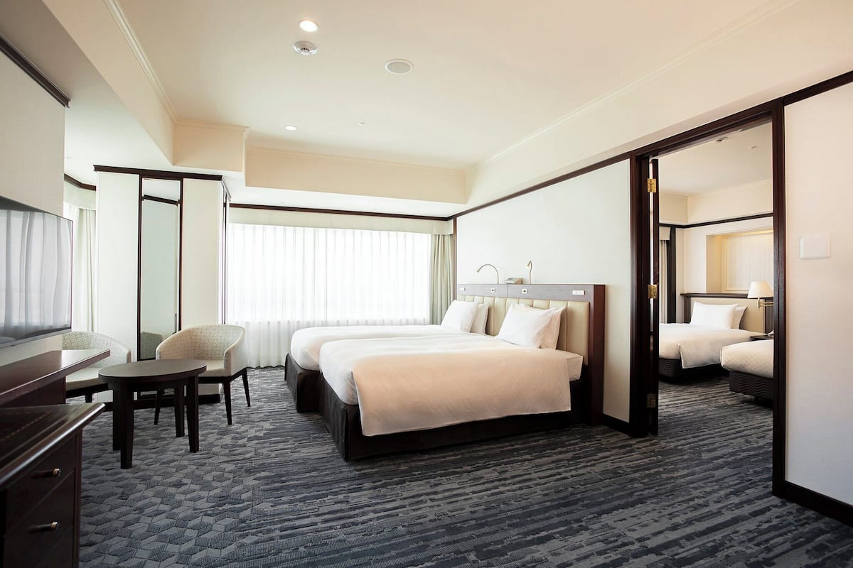 A hotel room with two beds, a desk, a chair, and a large mirror.