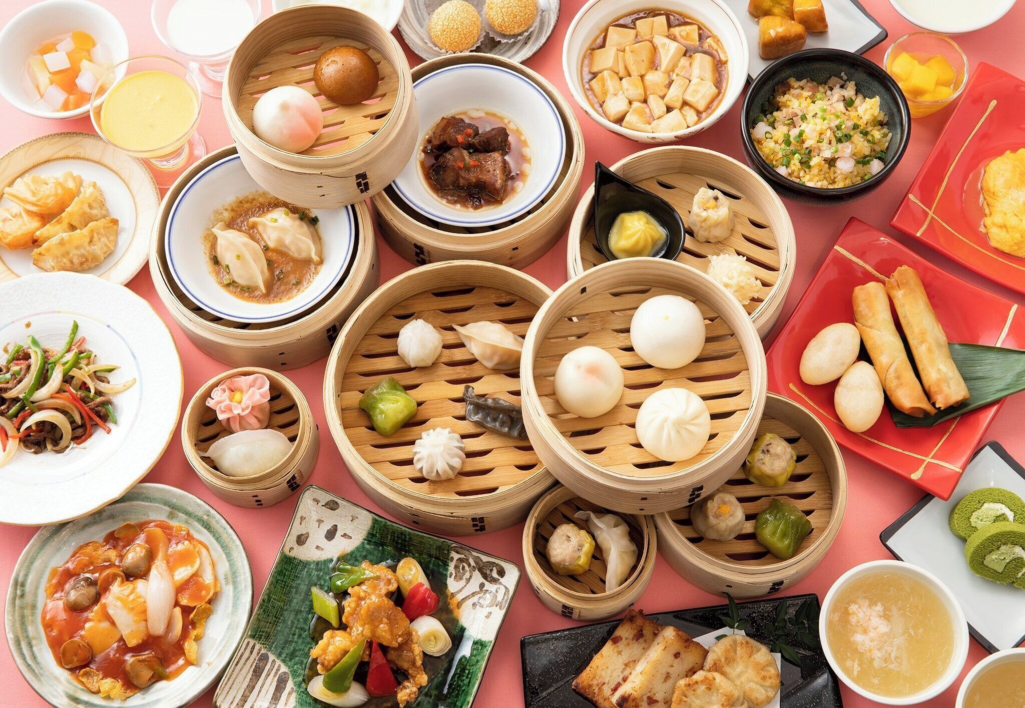 A variety of Asian dishes, including dumplings, tofu, and a bowl of soup, arranged on a pink table.