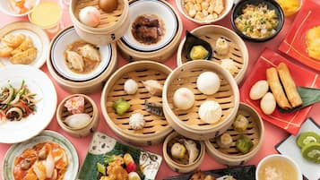 A variety of Asian dishes, including dumplings, tofu, and a bowl of soup, arranged on a pink table.