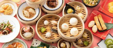 A variety of Asian dishes, including dumplings, tofu, and a bowl of soup, arranged on a pink table.