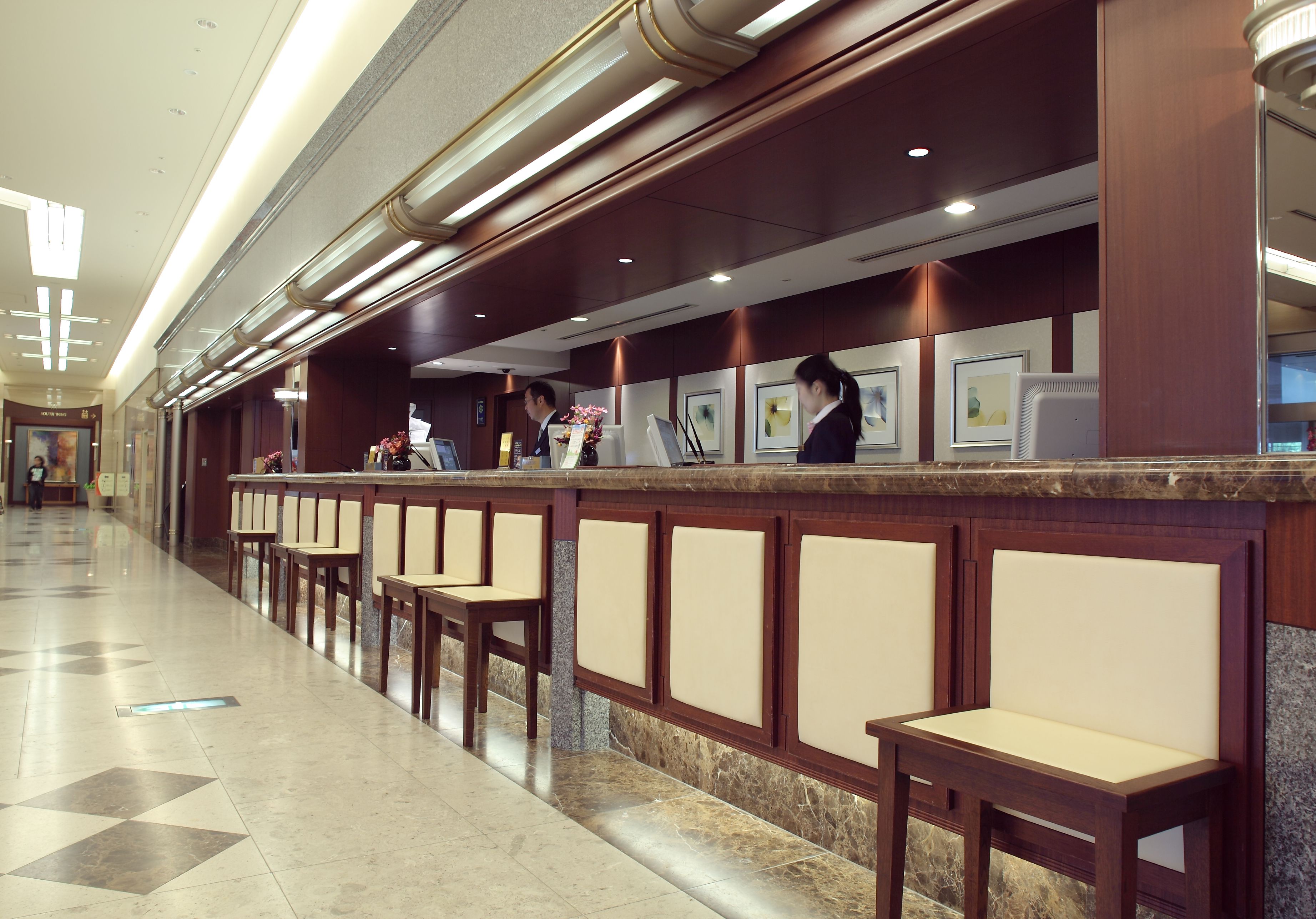 A hotel reception area with a marble floor, wooden reception desk, and cushioned seating.