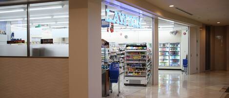 A clean, well-lit pharmacy with a blue sign, a refrigerated section, and a self-service beverage cooler.