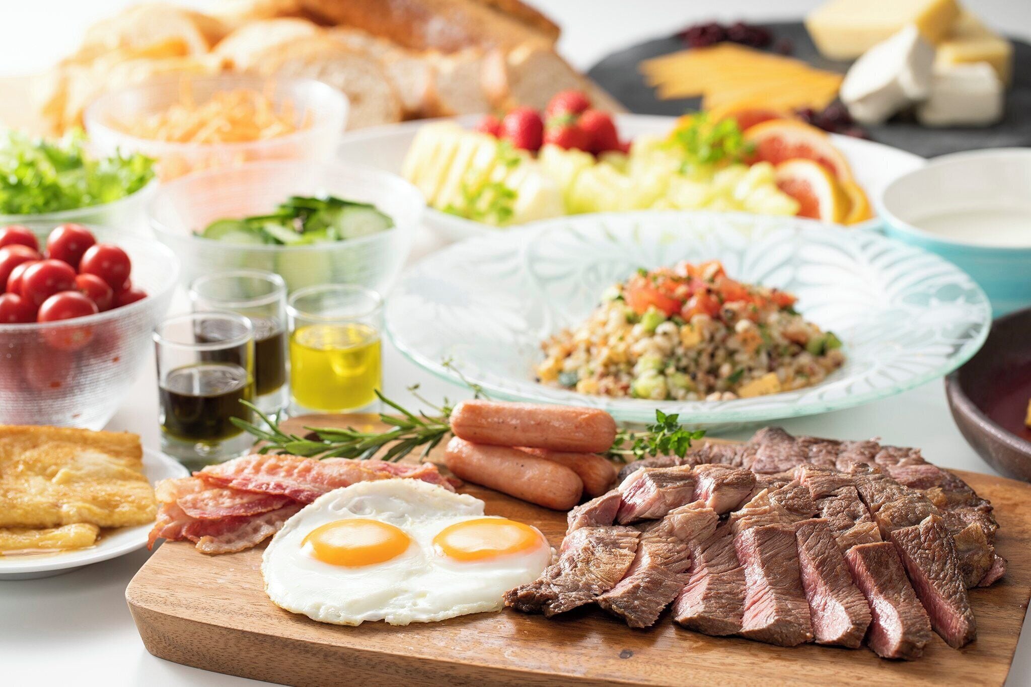 A breakfast spread with various dishes including eggs, steak, sausages, and a salad.