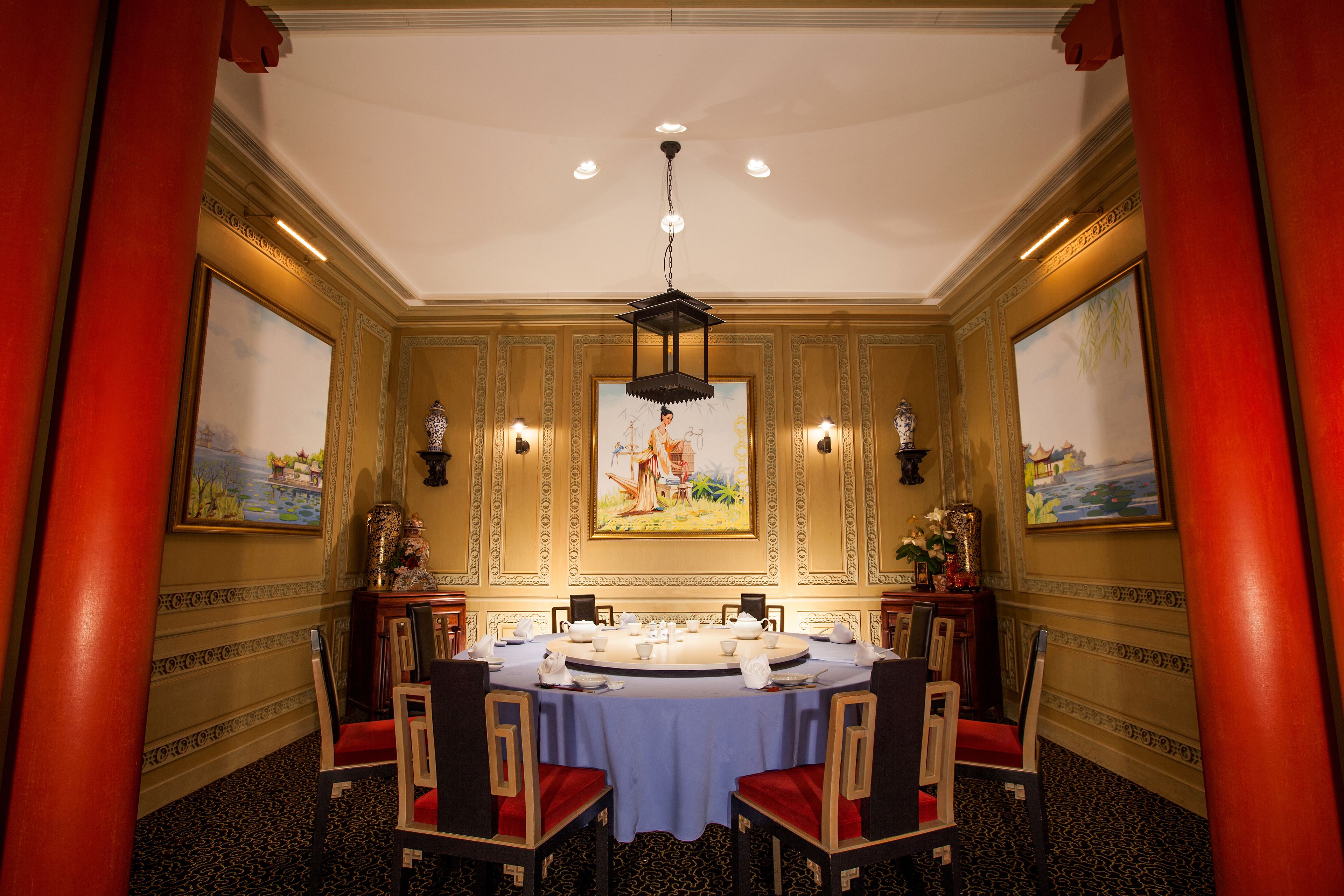 A formal dining room with a round table, chairs, and paintings on the walls.