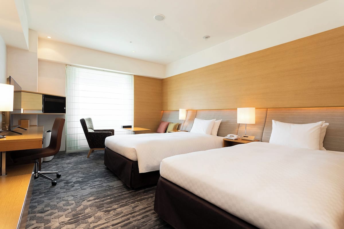 A hotel room with two beds, a desk, a chair, and a TV.