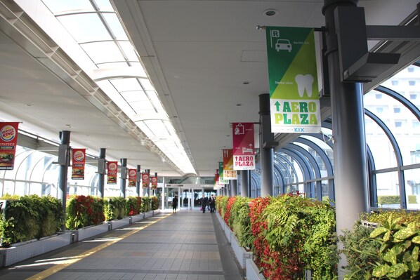A corridor with a glass ceiling, signs for 'AERO PLAZA' and 'Dental clinic', and a Burger King sign.