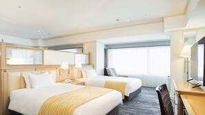 Ein Hotelzimmer mit zwei Betten, einem Schreibtisch, einem Stuhl, einem Fernseher und einem Fenster mit Vorhängen.