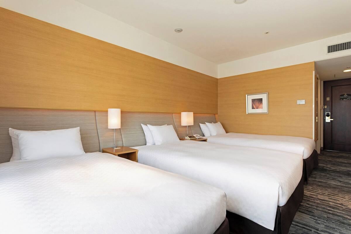 A hotel room with two beds, a wooden headboard, a framed picture on the wall, and a door with a keypad lock.