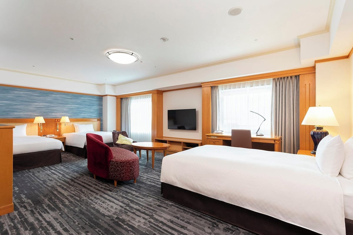 A hotel room with two beds, a desk, a TV, and a seating area.