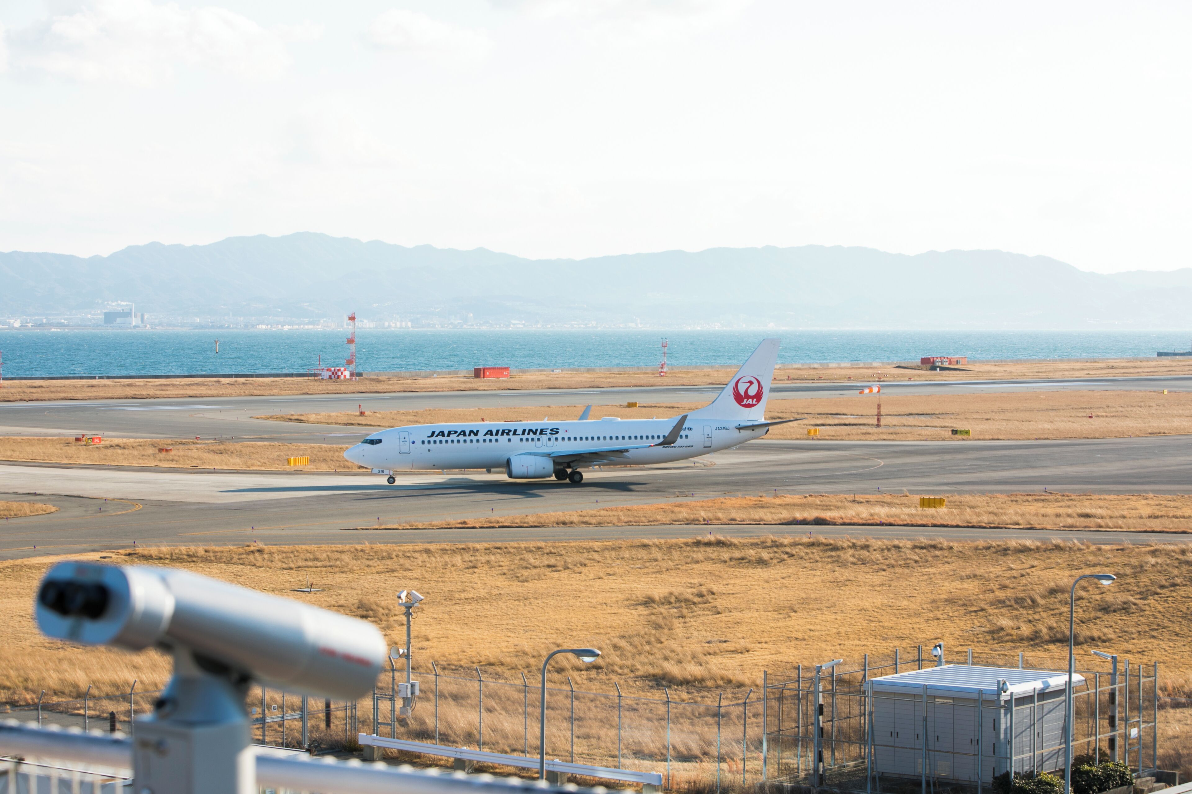 A Japan Airlines airplane on the runway with a mountainous backdrop.