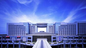 Ein modernes Hotel mit einer zentralen Glasfassade, mehreren Stockwerken und einem markanten Eingang.