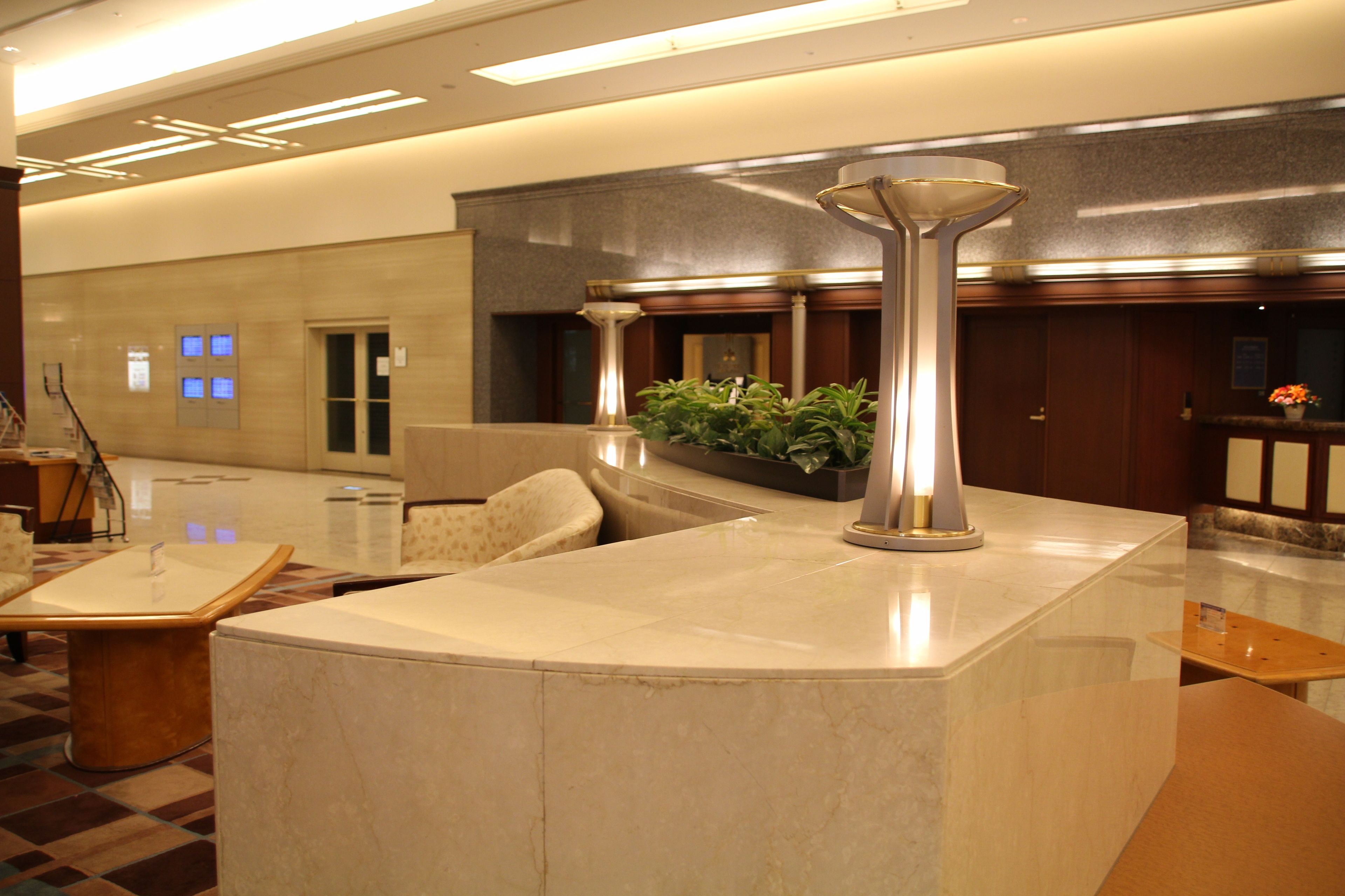 A lobby with a marble reception desk, a potted plant, and a large vase.