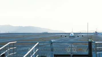 An airport runway with airplanes, including a large white one in the foreground, and distant mountains.