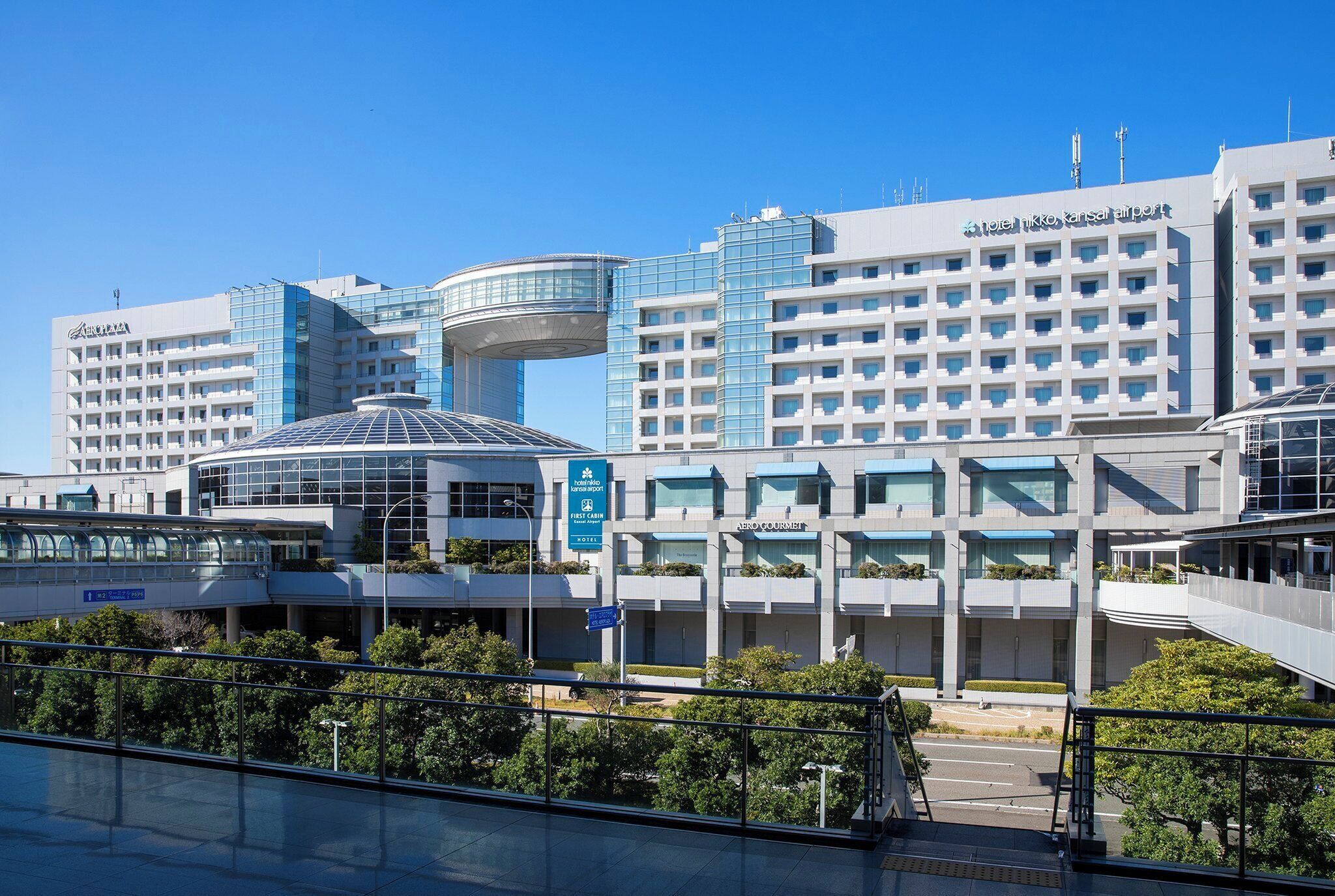 Un hotel moderno con una struttura circolare in vetro caratteristica, diversi piani e una segnaletica ben visibile.