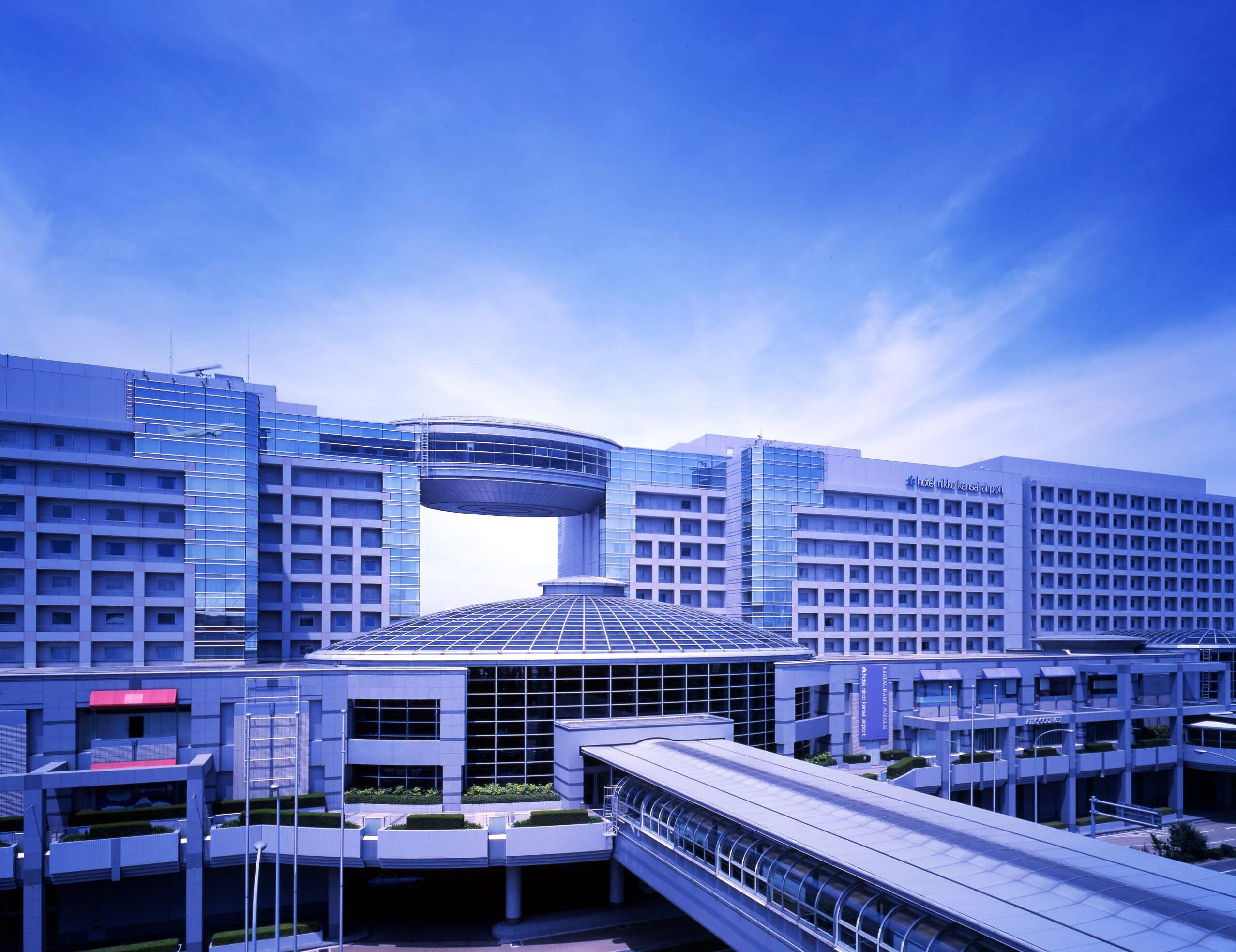 A modern hotel with a distinctive curved glass facade, a central atrium, and a rooftop garden.