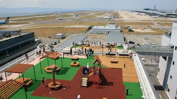An airport playground with green turf, wooden benches, and play structures.