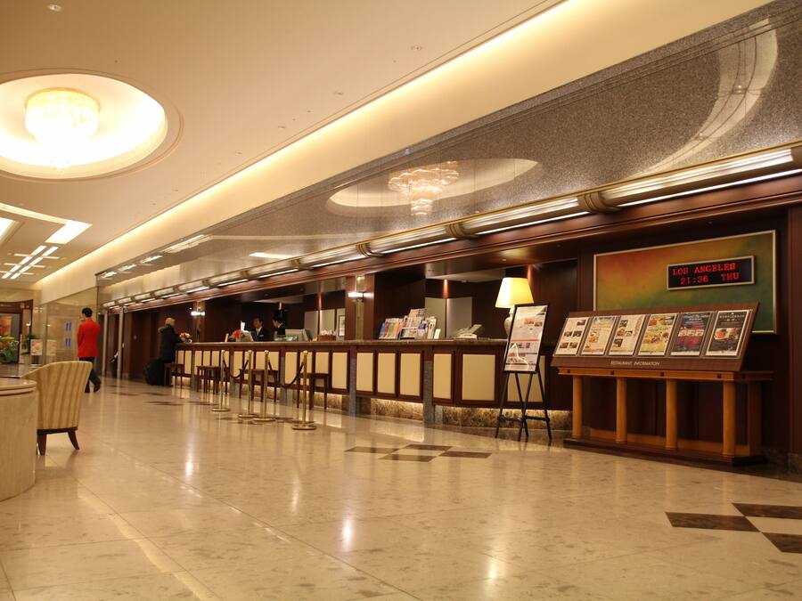 Et hotellets reception område med et marmorgulv, en receptionsdisk og et digitalt ur, der viser tid og dato.