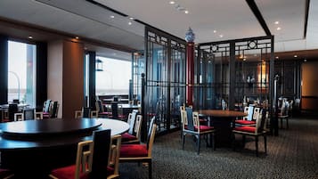 Un restaurante con mesas y sillas redondas, una alfombra estampada y un separador decorativo con un florero encima.
