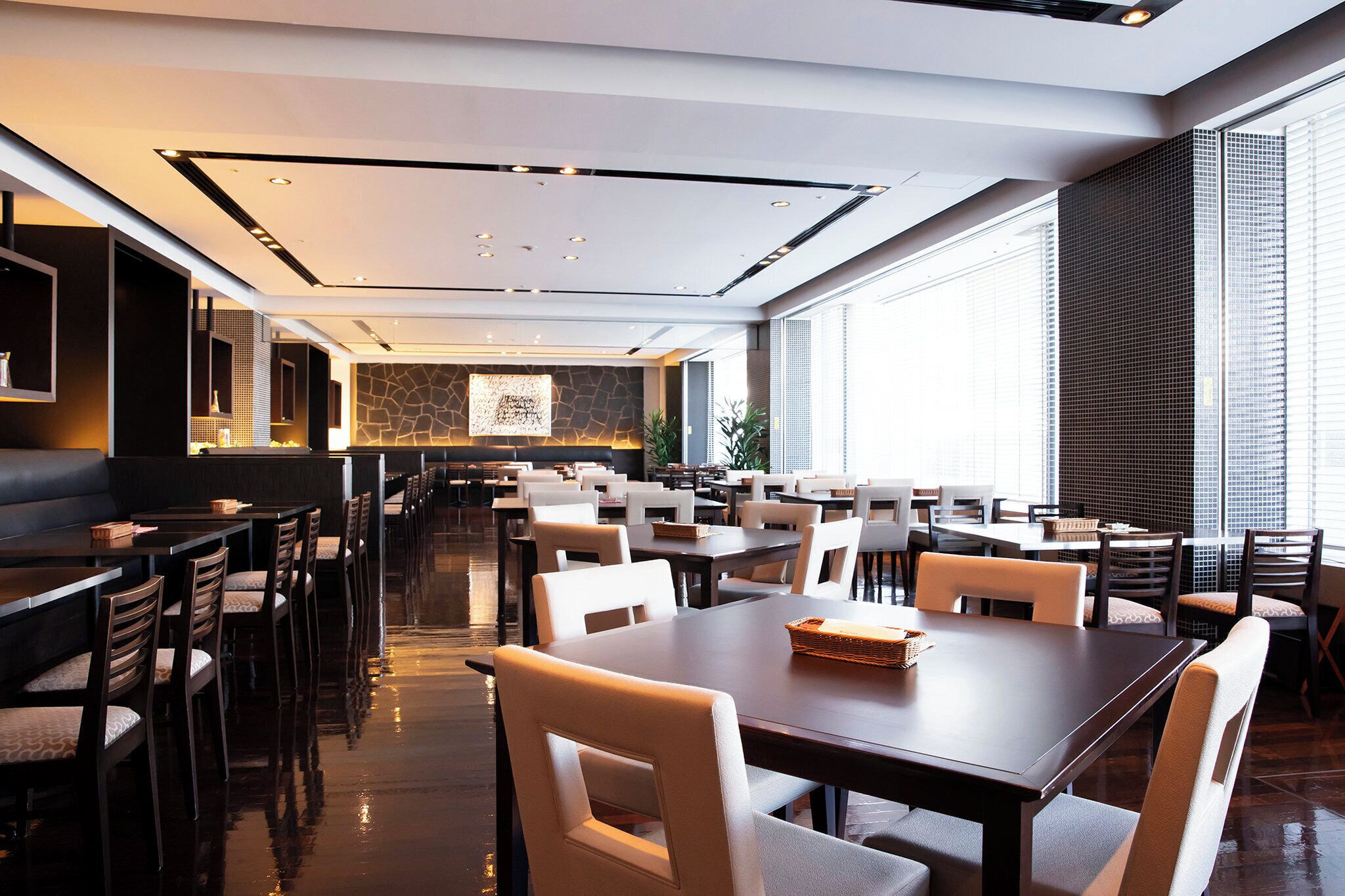 Un área de comedor moderna con varias mesas y sillas, una pared de acento de piedra y ventanas amplias que proporcionan luz natural.