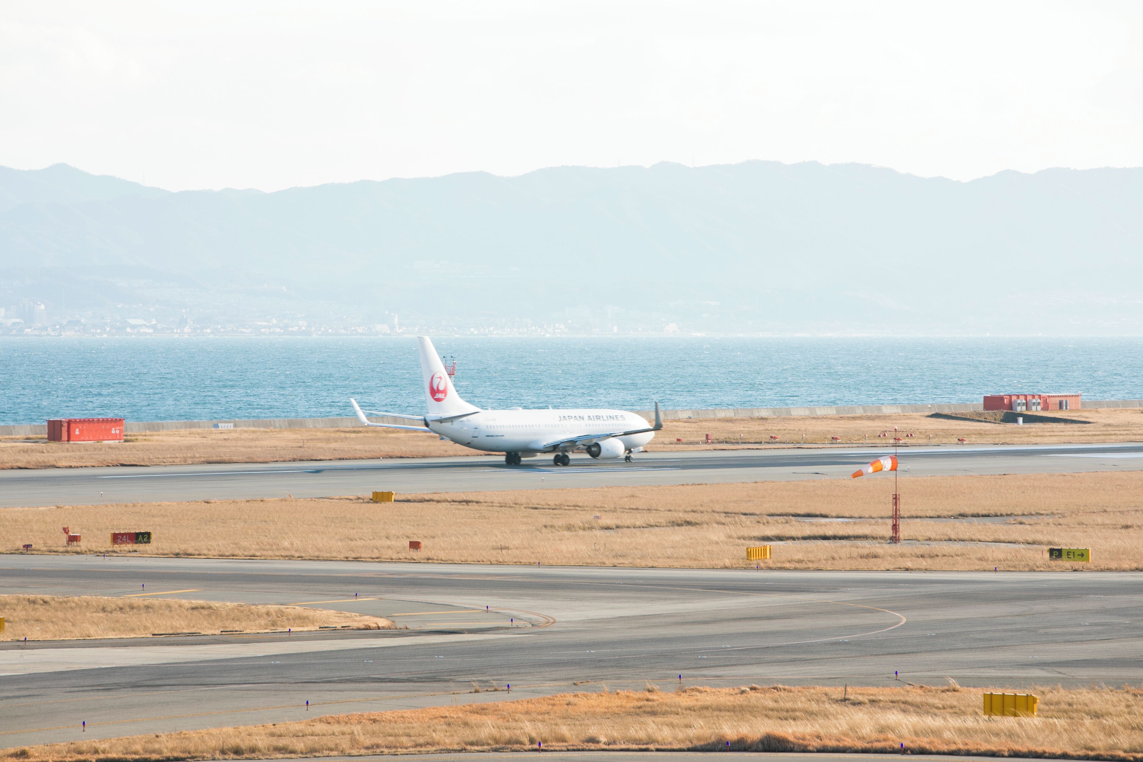 A Japan Airlines airplane on a runway with dry grass fields and mountains in the background.