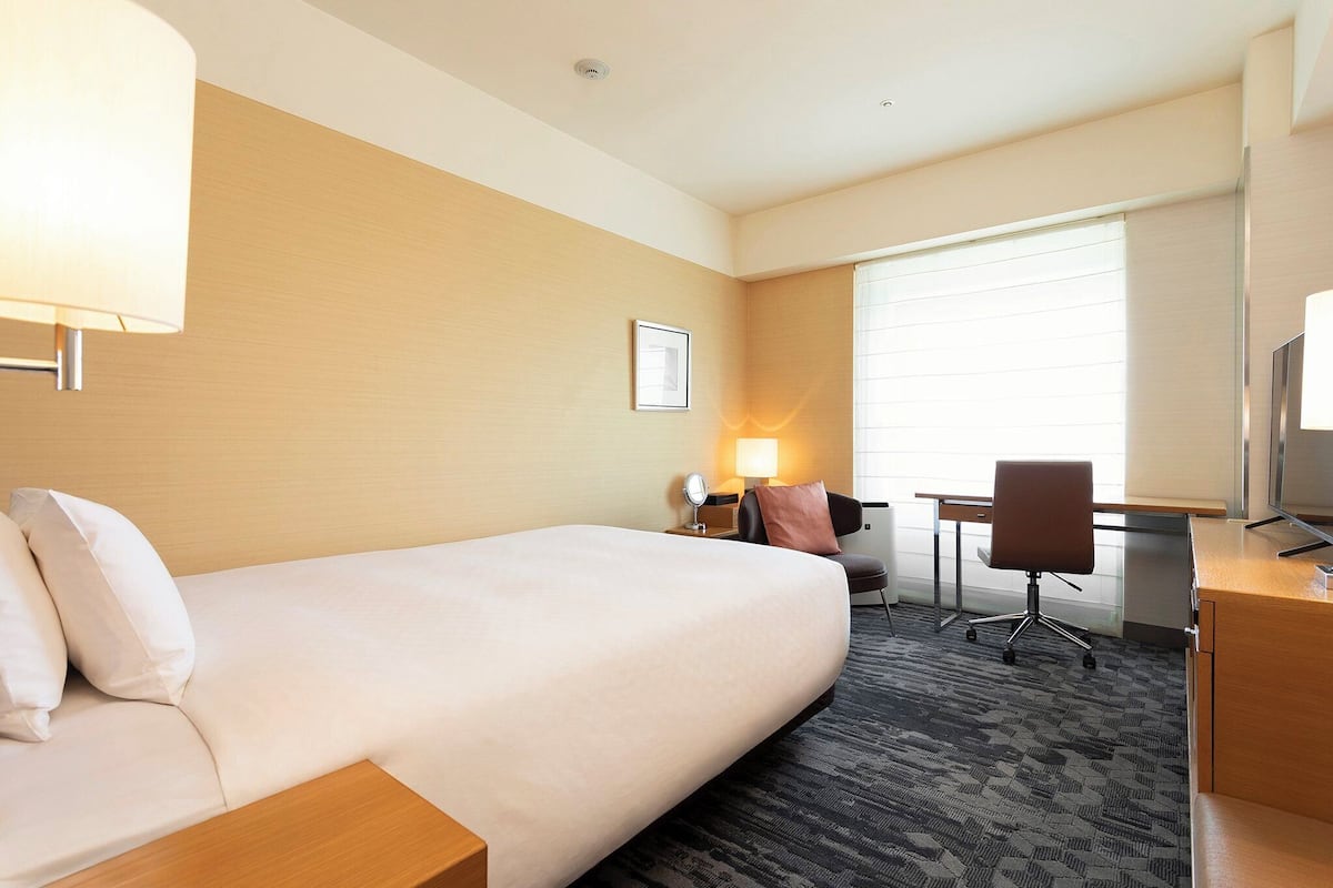 A hotel room with a large bed, a desk, a chair, and a TV.