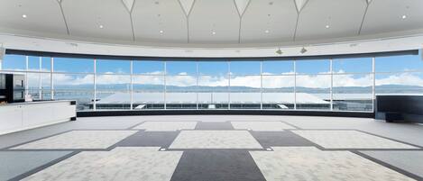 A spacious, modern room with a large panoramic window offering a view of the sky and distant mountains.