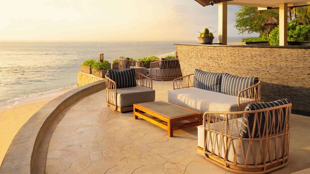 A coastal outdoor seating area with wicker furniture, a stone wall, and a view of the sea. - Hilton Bali Resort (Nusa Dua)