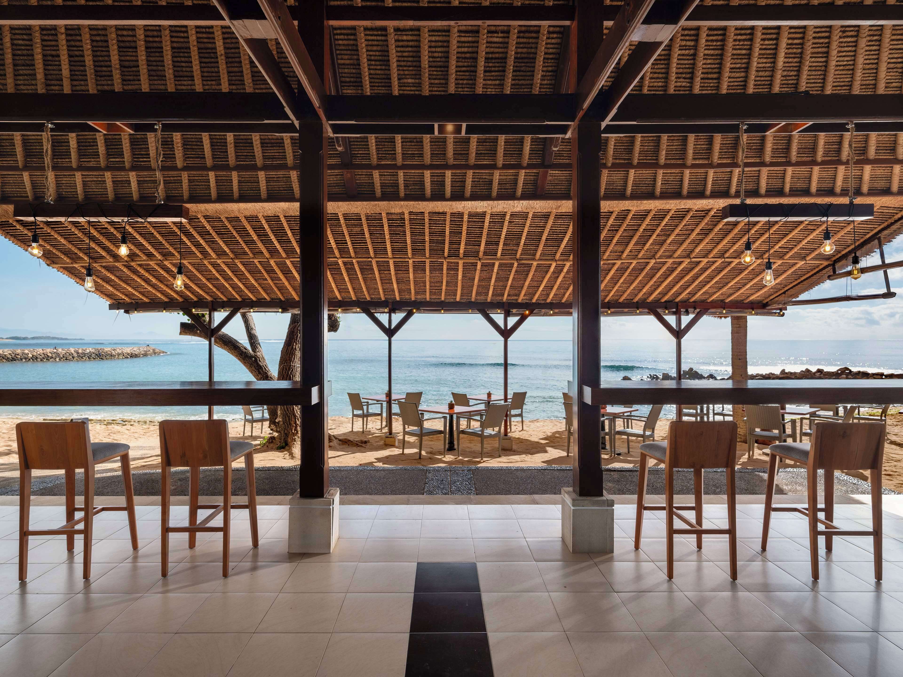 An outdoor seating area with tables and chairs, overlooking a beach and the ocean.