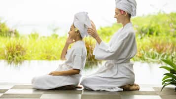 Dos personas con túnicas blancas sentadas sobre un suelo a cuadros, con vistas a zonas verdes y un cuerpo de agua al fondo.