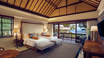 A spacious bedroom with a large bed, a smaller bed, and a seating area with a table and chairs. There is a balcony with a view of the ocean.