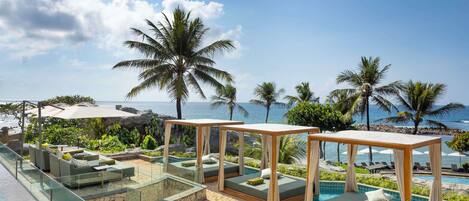 Zona de piscina en un resort con asientos, una barrera de cristal y vistas al océano.