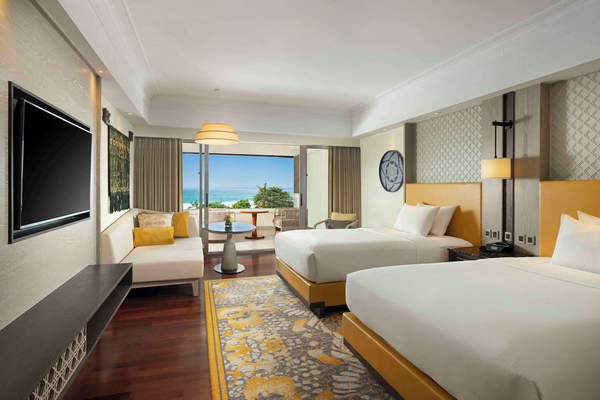 Ein Hotelzimmer mit zwei Betten, einem Fernseher, einem kleinen Tisch und Blick aufs Meer.