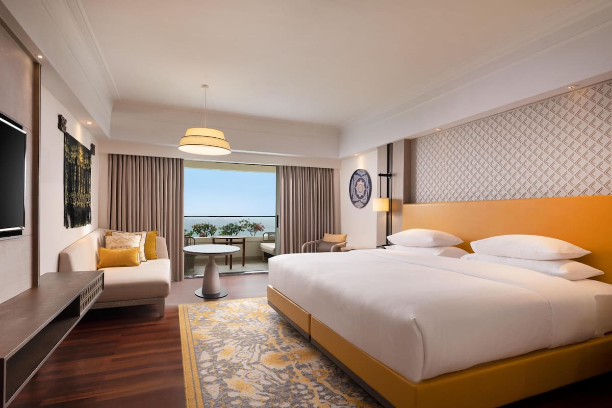Ein Hotelzimmer mit einem großen Bett, einem Schreibtisch, einem Stuhl, einem kleinen Tisch und einem Balkon mit Blick.