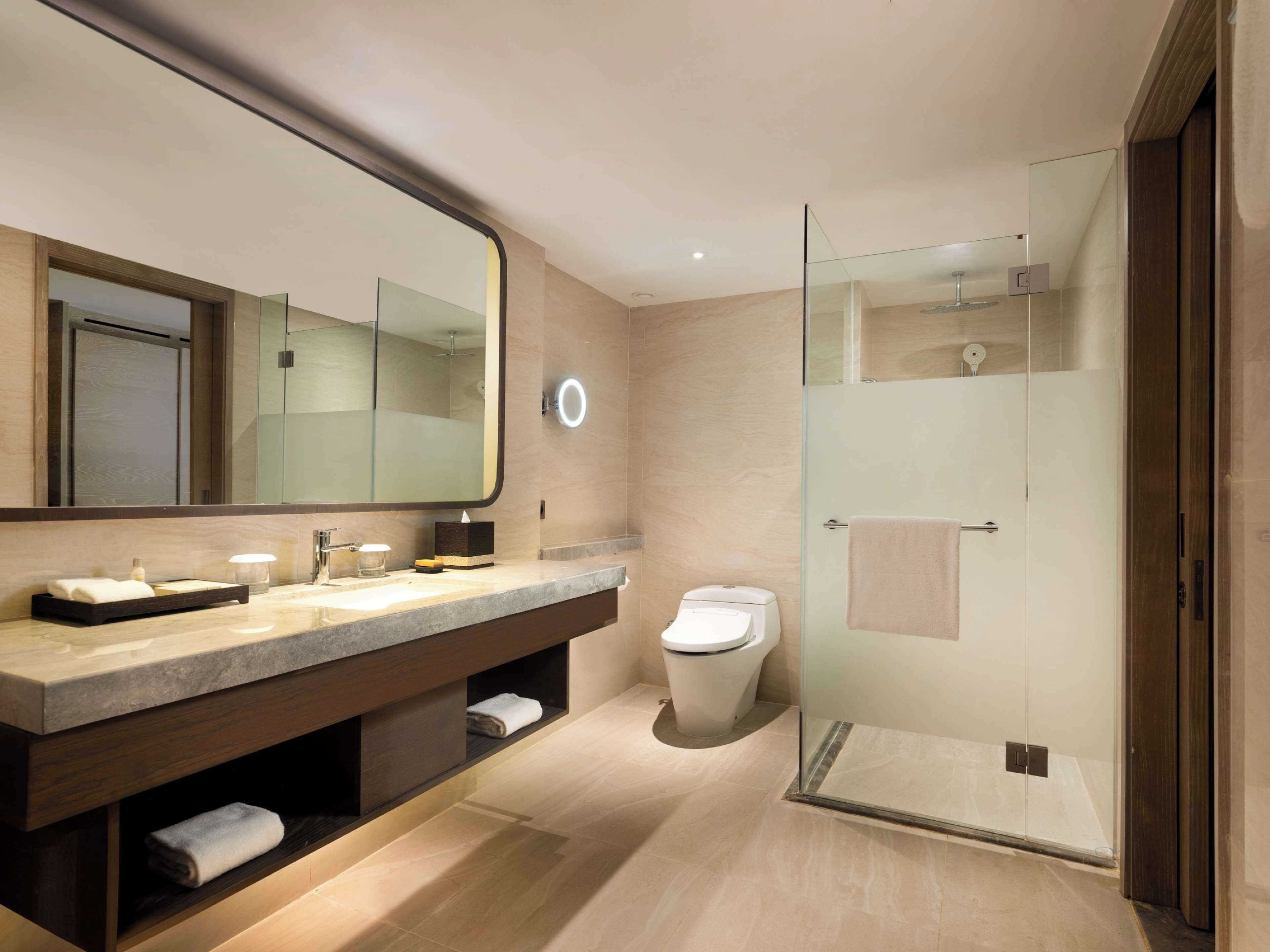 Un baño moderno con un espejo grande, un tocador con lavamanos, un inodoro y una ducha con mampara de vidrio.
