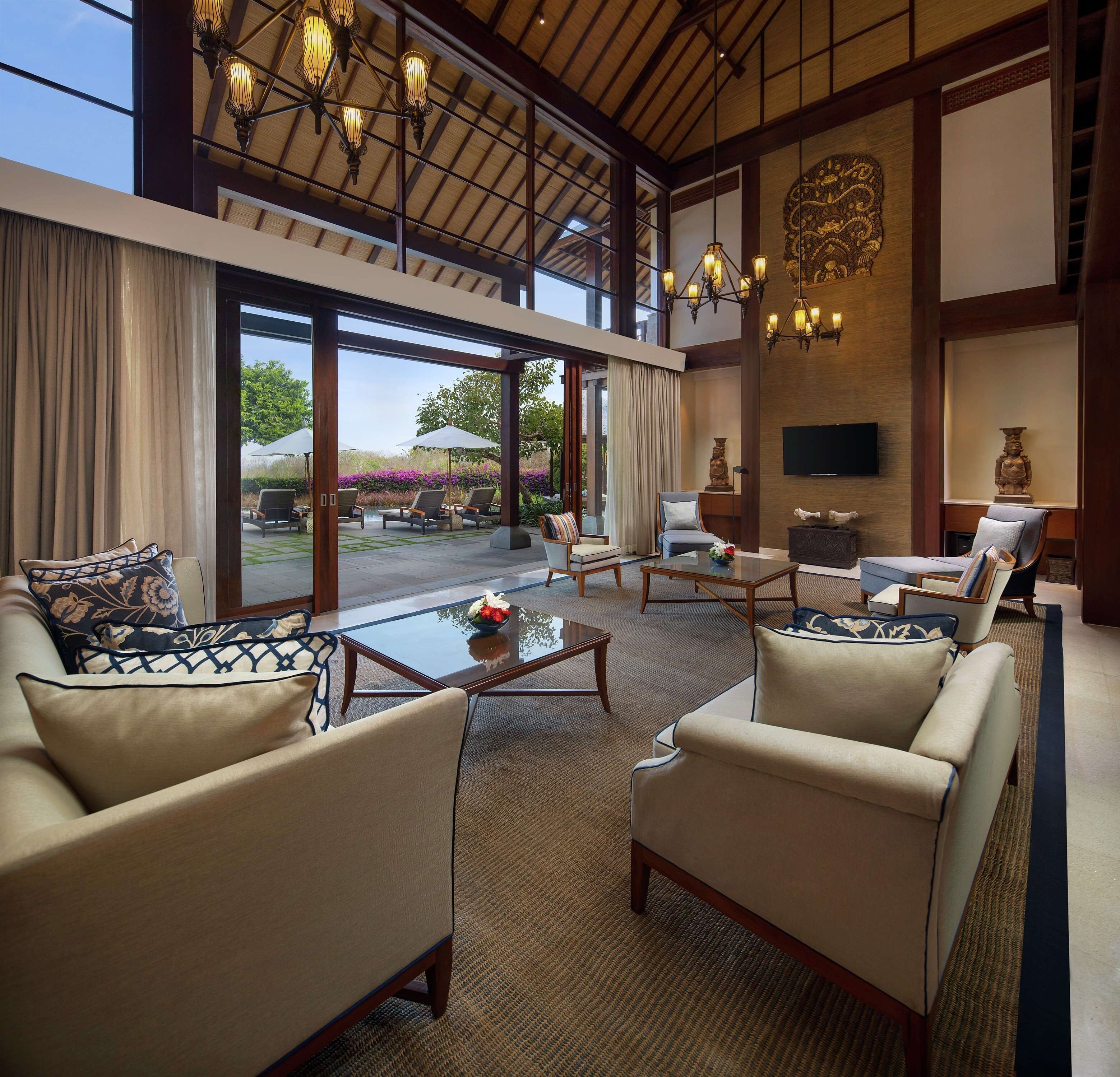 A spacious indoor area with a high ceiling, large windows, and a view of the outdoors. There are several seating areas with sofas and chairs, a coffee table, and decorative items.