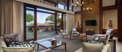 A spacious indoor area with a high ceiling, large windows, and a view of the outdoors. There are several seating areas with sofas and chairs, a coffee table, and decorative items.