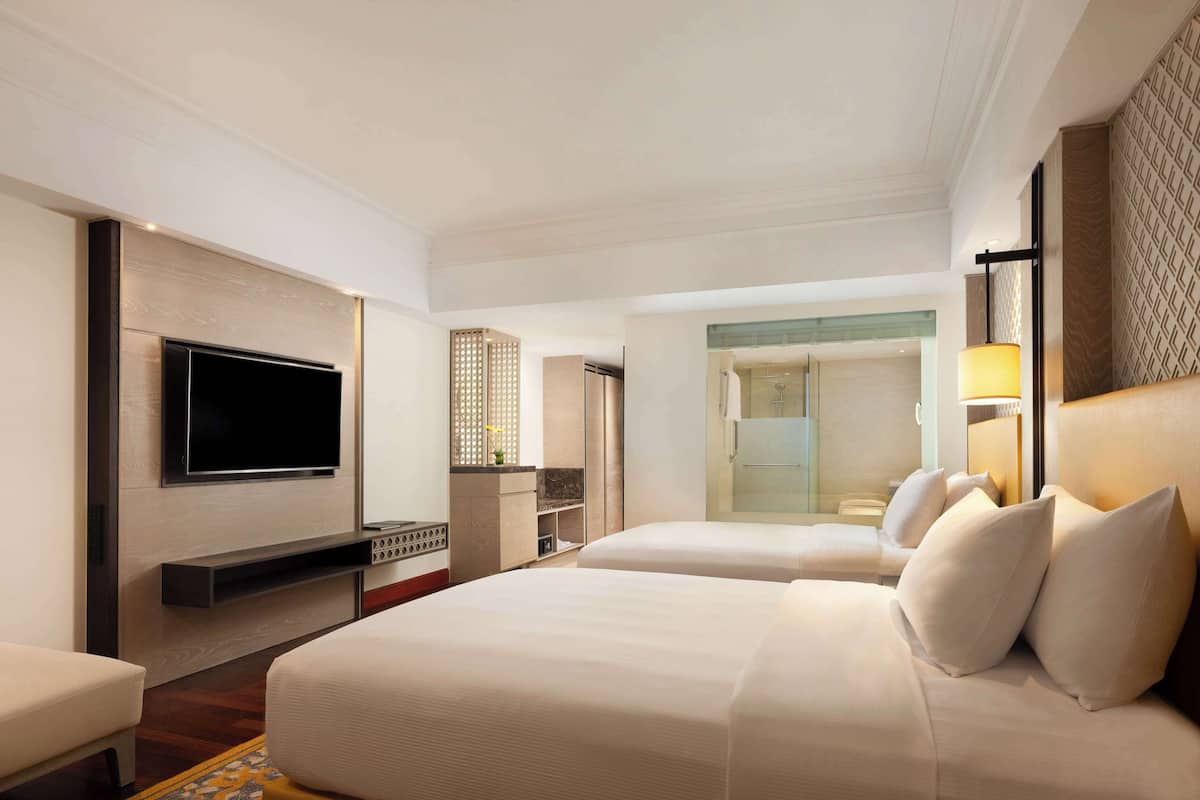 Ein Hotelzimmer mit einem großen Bett, einem an der Wand montierten Fernseher, einem Schreibtisch mit Computer und einem begehbaren Kleiderschrank.