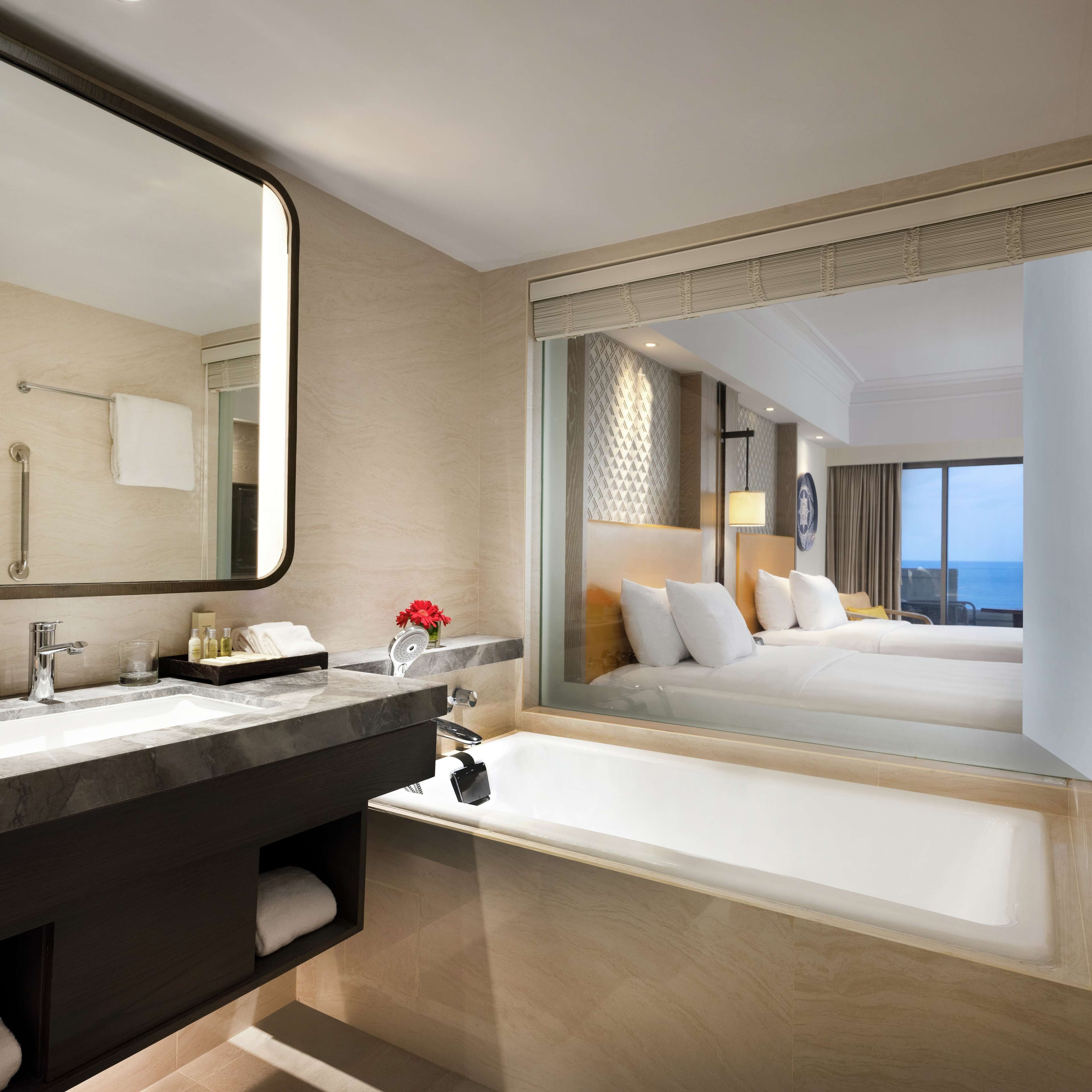 A modern hotel bathroom with a large mirror, a bathtub, a vanity with a sink, and a shower.