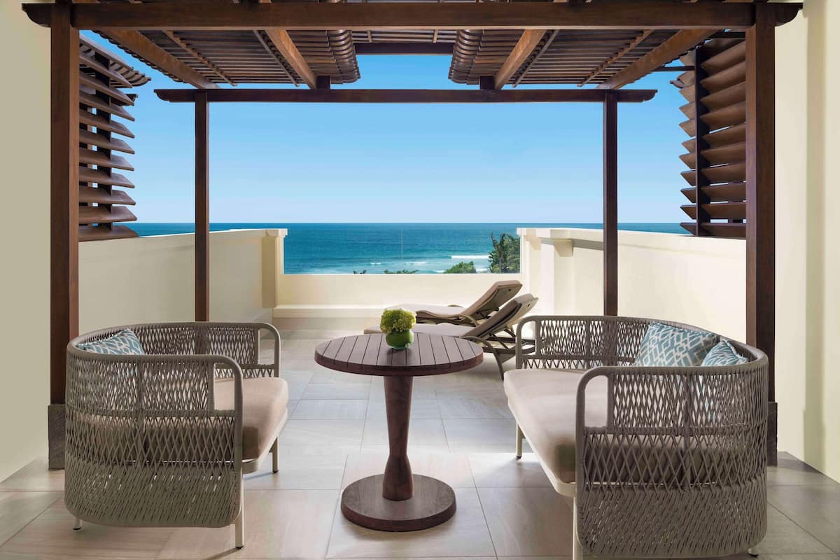 Ein Balkon mit Korbmöbeln, einem runden Tisch und Blick aufs Meer.