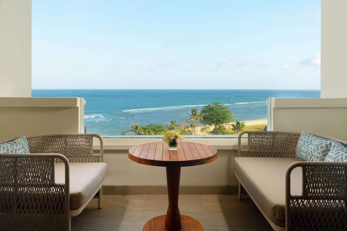 Ein Balkon mit Korbmöbeln und einem Holztisch mit Blick auf Strand und Meer.
