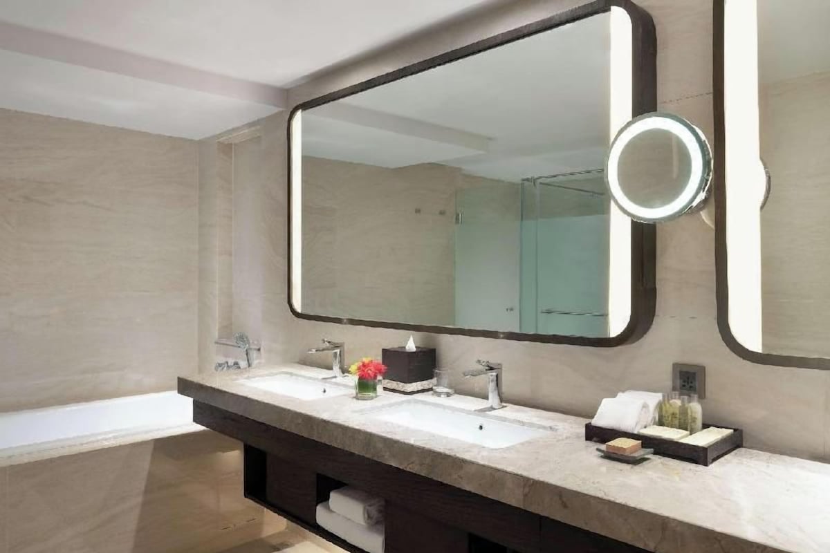 A modern bathroom with a large mirror, two sinks, and a bathtub.