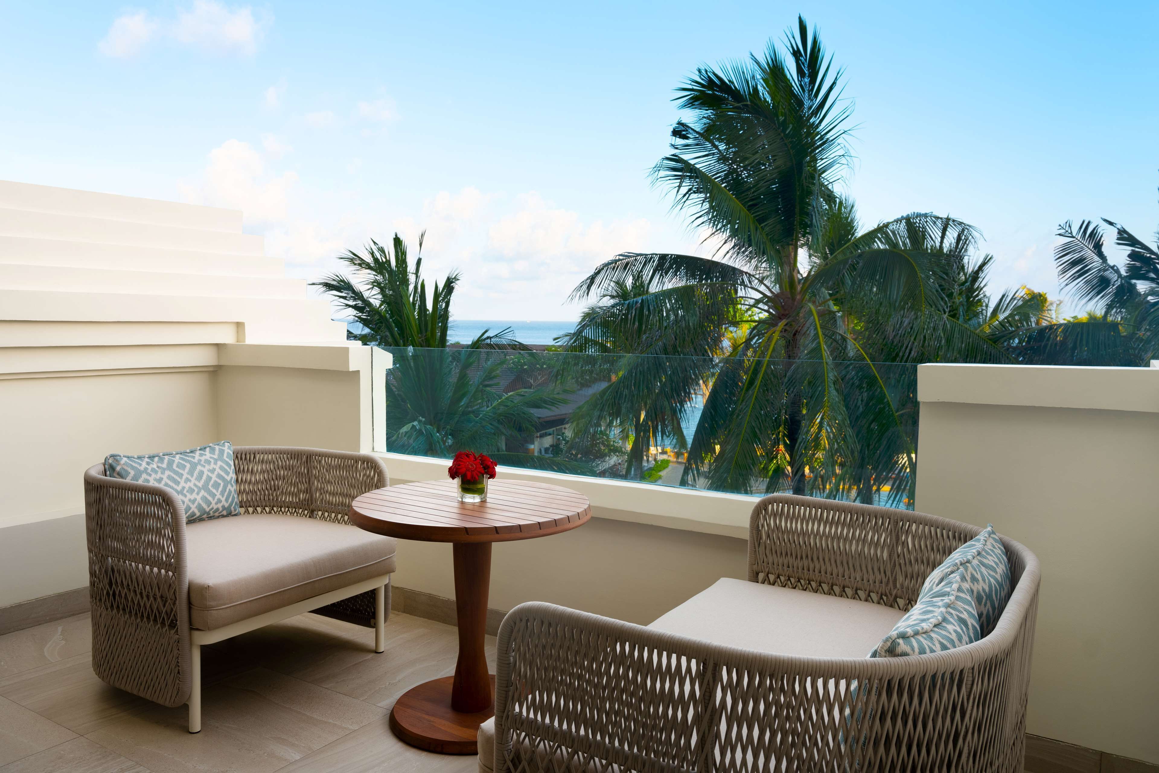 A balcony with wicker furniture, a small round table, and a vase of red flowers.